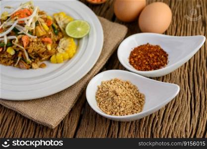 Pad Thai in a white plate with lemon, eggs and seasoning on a wooden table. Selective focus