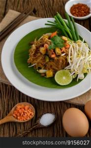 Pad Thai in a white plate with lemon, eggs and seasoning on a wooden table. Selective focus