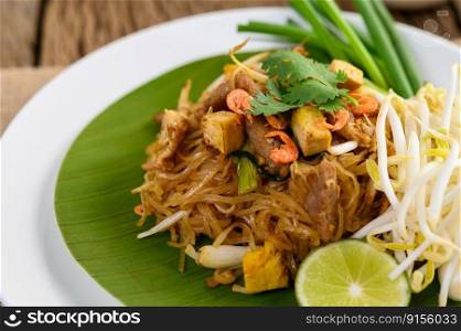 Pad Thai in a white plate with lemon on a wooden table