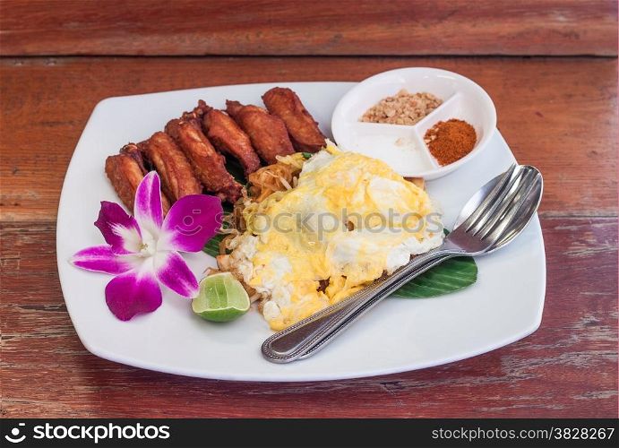 Pad thai with fried chicken wing and egg in white plate on wooden table