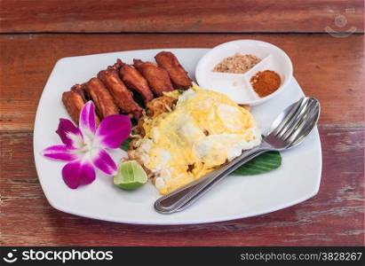 Pad thai with fried chicken wing and egg in white plate on wooden table