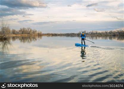 Paddling stand up paddleboard on a calm lake, early spring scenery in northern Colorado