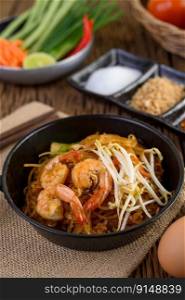 Padthai shrimp in a black bowl with eggs and Seasoning on wooden table.