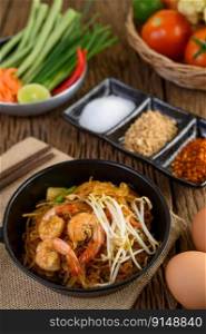 Padthai shrimp in a black bowl with eggs and Seasoning on wooden table.