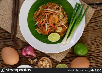 Padthai shrimp in a white dish with lime and eggs on wooden table.