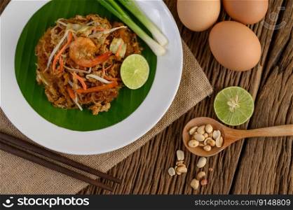Padthai shrimp in a white dish with lime and eggs on wooden table.