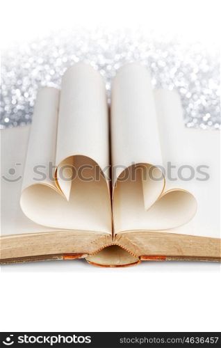 Pages of open book rolled in heart shape on glitter background