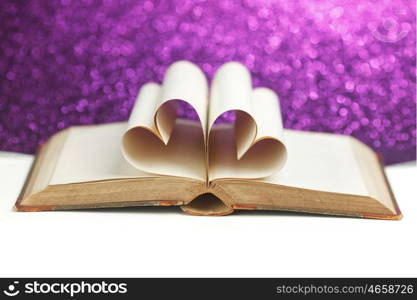 Pages of open book rolled in heart shape on glitter background