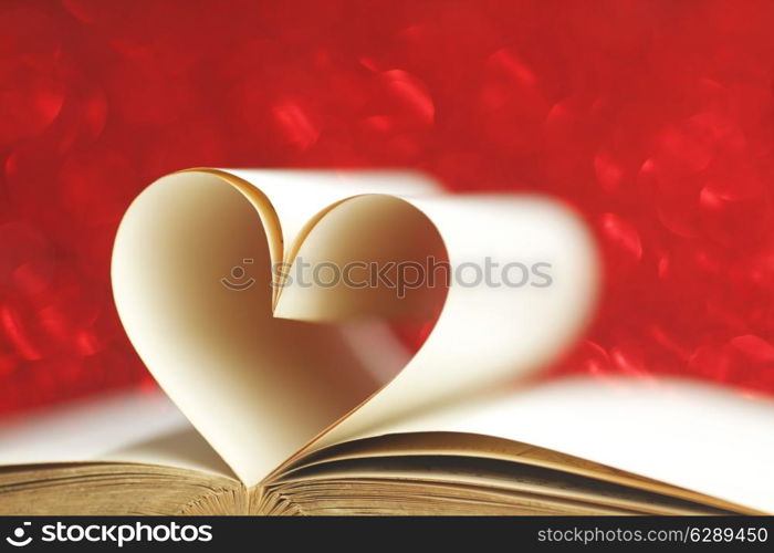 Pages of open book rolled in heart shape on glitter background