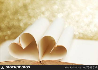 Pages of open book rolled in heart shape on glitter background
