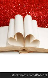 Pages of open book rolled in heart shape on glitter background. Pages in heart shape