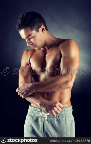 pain relief, sport, bodybuilding, health and people concept - young man standing over black background