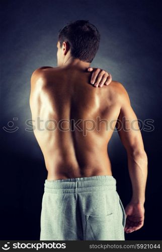 pain relief, sport, bodybuilding, strength and people concept - young man standing over black background
