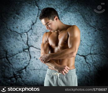 pain, sport, bodybuilding, health and people concept - young male bodybuilder touching injured elbow over concrete wall background