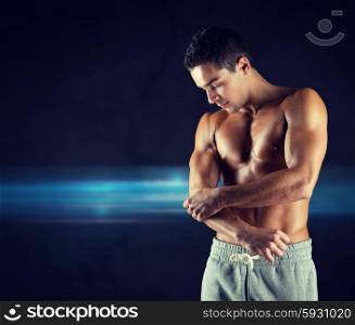 pain, sport, bodybuilding, health and people concept - young male bodybuilder touching injured elbow over dark background