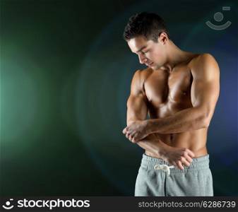 pain, sport, bodybuilding, health and people concept - young male bodybuilder touching injured elbow over dark background