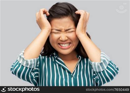 pain, stress and despair concept - stressed asian woman having headache holding to her head over grey background. stressed asian woman holding to her head