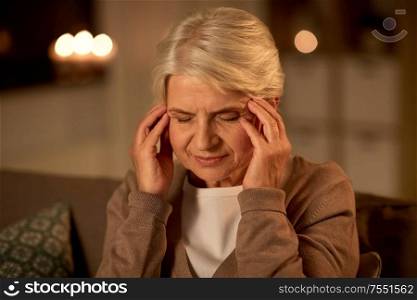 pain, stress and people concept - unhappy senior woman suffering from headache at home at night. unhappy senior woman suffering from headache