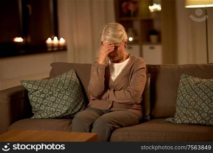 pain, stress and people concept - unhappy senior woman suffering from headache at home at night. unhappy senior woman suffering from headache