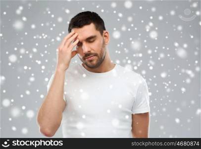 pain, stress, winter, christmas and people concept - young man suffering from headache over snow on gray background