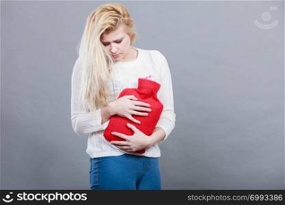 Painful periods and menstrual cramp problems concept. Woman having stomach cramps feeling very unwell holding hot water bottle.. Woman feeling stomach cramps holding hot water bottle