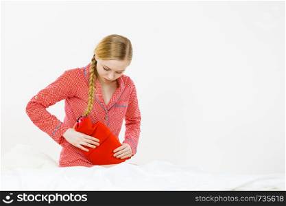 Painful periods and menstrual cramp problems concept. Woman having stomach cramps lying on bed holding hot water bottle feeling very unwell.. Woman feeling stomach cramps lying on bed