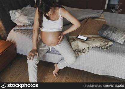 Painful pregnant young woman at home calling medical assistance on phone 