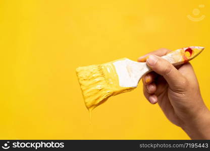 Paint brush, close up hand painter worker painting on surface wall Painting apartment, renovating with yellow color paint. Leave empty copy space to write descriptive text beside.