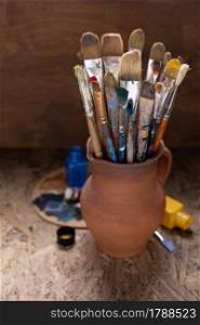 Paint brush in clay jug and palette on table background texture. Paintbrush for painting as artistic still life. Abstract art concept