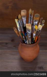 Paint brush in clay jug on wooden table background texture. Paintbrush for painting as artistic paint still life. Abstract art concept