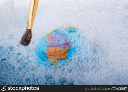 Paint brush placed on the top of globe in a water covered with foam