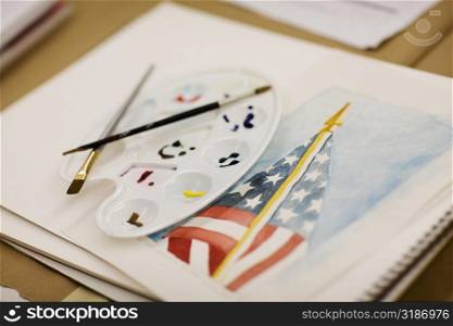 Paint brushes and a palette on an American flag painted on a sketch pad