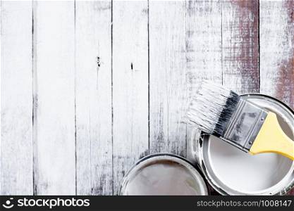 Paint brushes and canisters are placed on the wooden table surface painted with white.