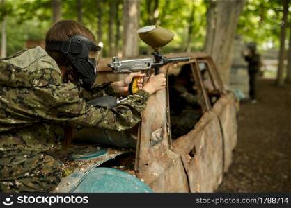 Paintball player in uniform and mask playing on playground in the forest. Extreme sport with pneumatic weapon and paint bullets or markers, military team game outdoors. Paintball player in uniform and mask in forest