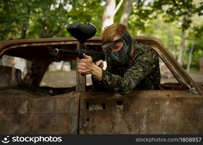 Paintball player in uniform and mask playing on playground in the forest. Extreme sport with pneumatic weapon and paint bullets or markers, military team game outdoors, combat tactics. Paintball player in uniform and mask in forest