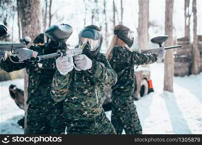 Paintball players in uniform and masks poses with marker guns in hands after winter forest battle. Extreme sport game. Paintball players in uniform and masks poses
