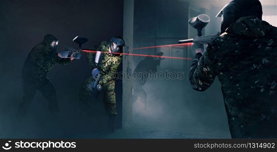 Paintball team in battle, guns with a laser sight. Extreme sport game, players in protection masks and camouflage holds weapon in hands