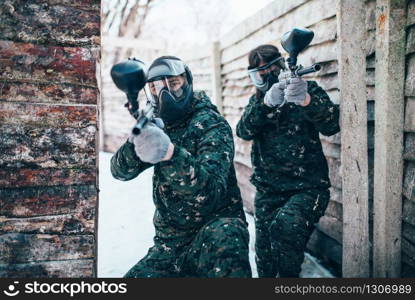 Paintball team, players in winter battle. Extreme sport game, soldiers in protection masks and camouflage holds weapon in hands. Paintball team, players in winter battle