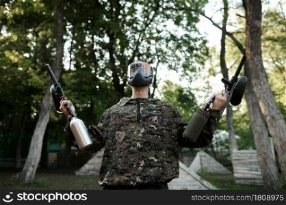 Paintball warrior with guns poses on playground in the forest. Extreme sport with pneumatic weapon and paint bullets or markers, military team game outdoors, combat tactics. Paintball warrior poses on playground in forest
