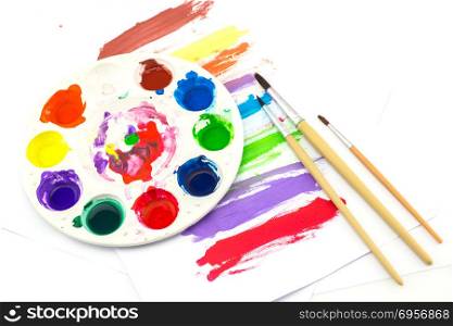 paintbrush lies on the palette with paints on white background