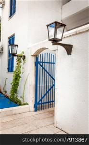Painted blue gates in white wall with gas lamp at greek style