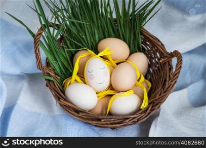 Painted Easter eggs, one egg with a cute face, eggs lie in a wooden basket along with green grass. Postcard for Easter. Painted Easter eggs, one egg with a cute face, eggs lie in a wooden basket along with green grass. Postcard for Easter.