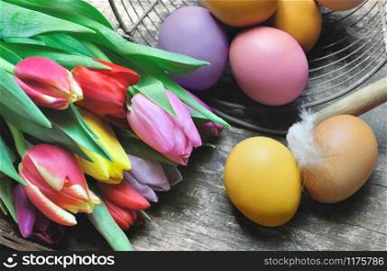painted eggs with bunch of tulips on wooden background