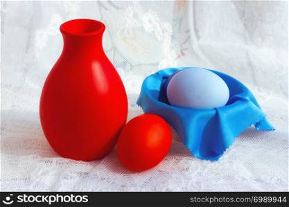 Painted red with blue Easter eggs and a ceramic jag on a white vintage lace tablecloth. Selective focus on the foreground.. Colorful Easter Eggs And A Jug On A Lace