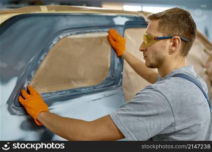Painter applying adhesive paper for car body protection during painting or polishing process. Painter applying adhesive paper for car protection