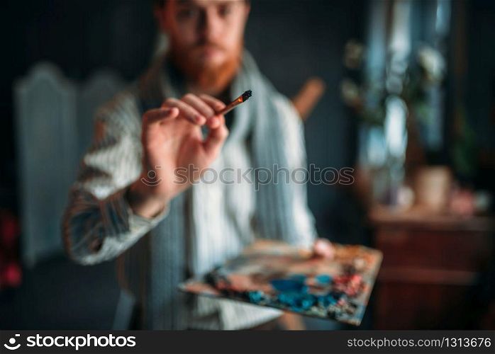 Painter with palette and brush in hand selective focus, art studio on background. Oil paint, paintbrush drawing