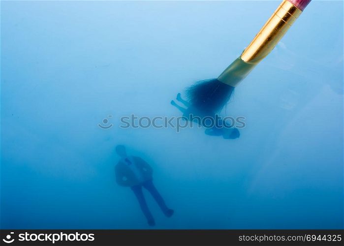 Painting brush and little floating figurines in blue water