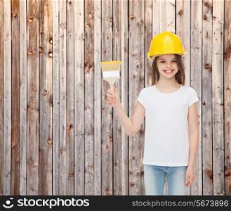 painting, building, childhood and people concept - smiling little girl in protective helmet with paint brush over wooden fence background