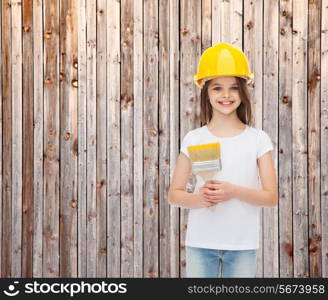 painting, building, childhood and people concept - smiling little girl in protective helmet with paint brush over wooden fence background