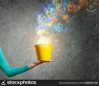 Painting concept. Close up of female hand holding bucket with colorful fumes